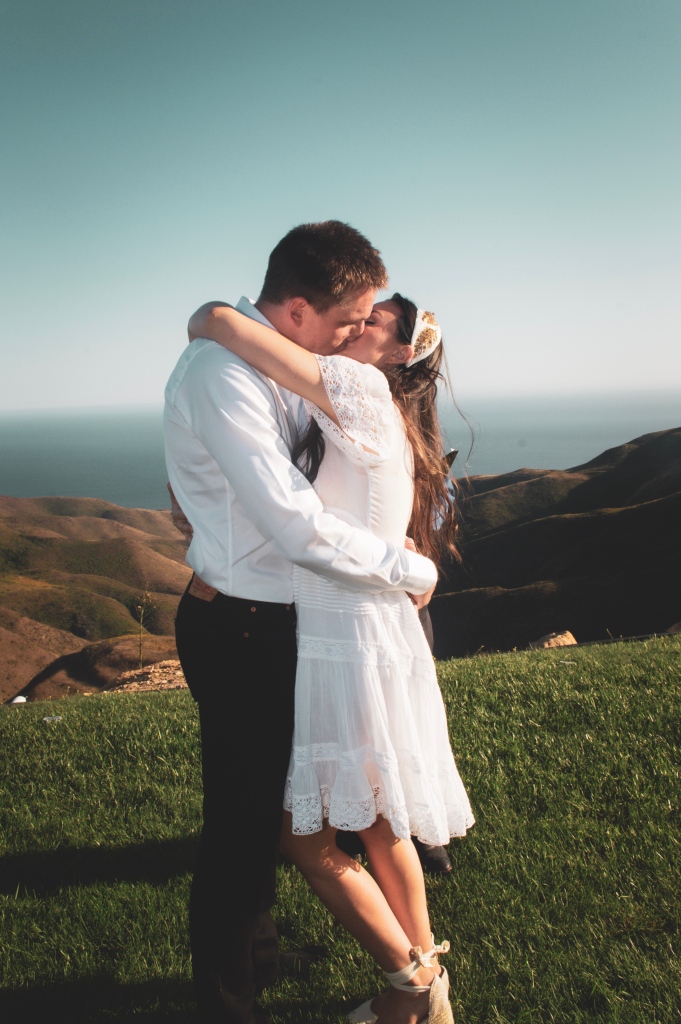 Married couple kissing on a cliff overlooking the ocean